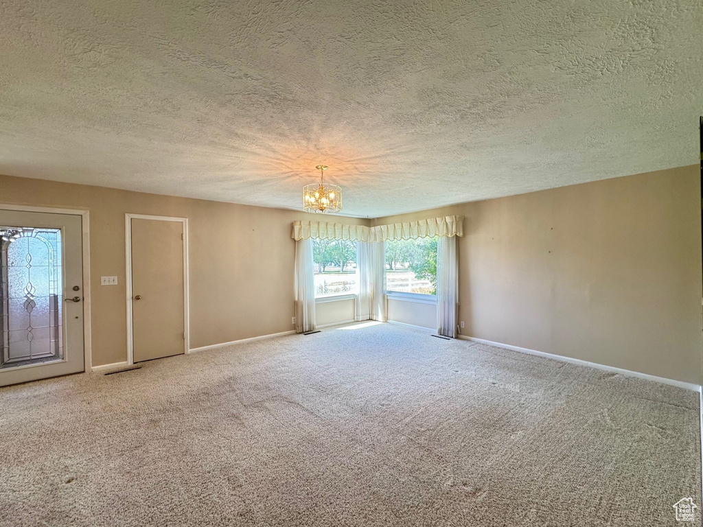 Unfurnished room featuring a notable chandelier, a textured ceiling, and carpet flooring