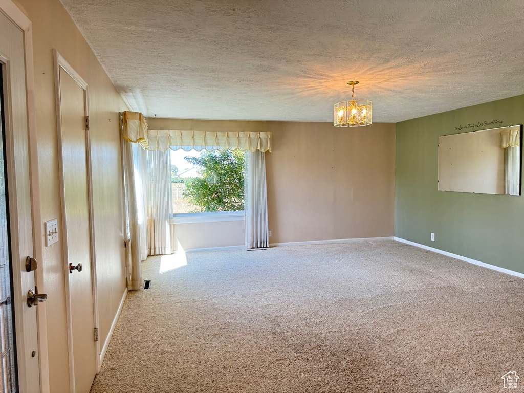 Unfurnished room with a notable chandelier, a textured ceiling, and carpet flooring