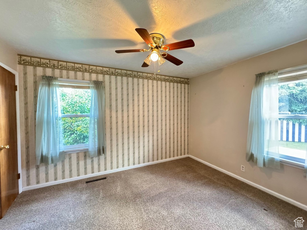 Empty room with a textured ceiling, carpet flooring, and ceiling fan