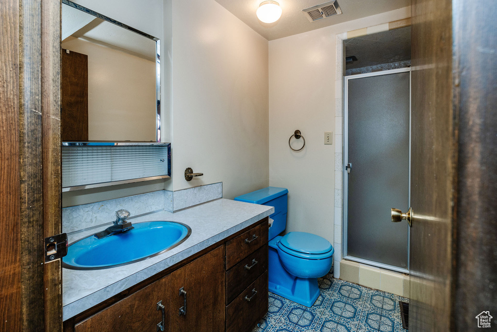 Bathroom with a shower with shower door, vanity, toilet, and tile patterned flooring