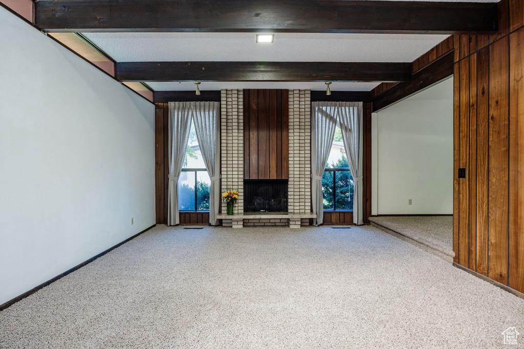 Unfurnished living room with wood walls, beamed ceiling, brick wall, and carpet floors