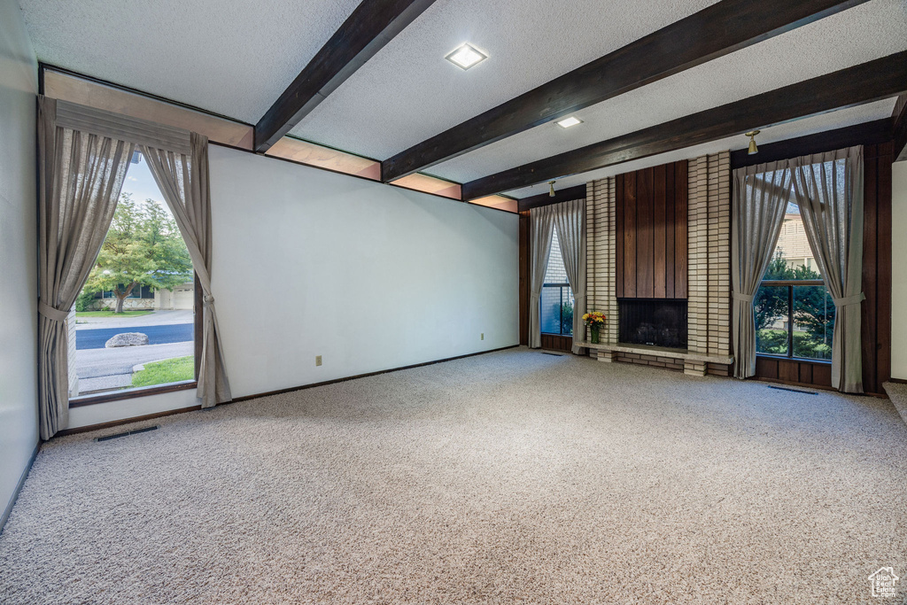 Unfurnished living room featuring carpet floors, a fireplace, a textured ceiling, and beam ceiling