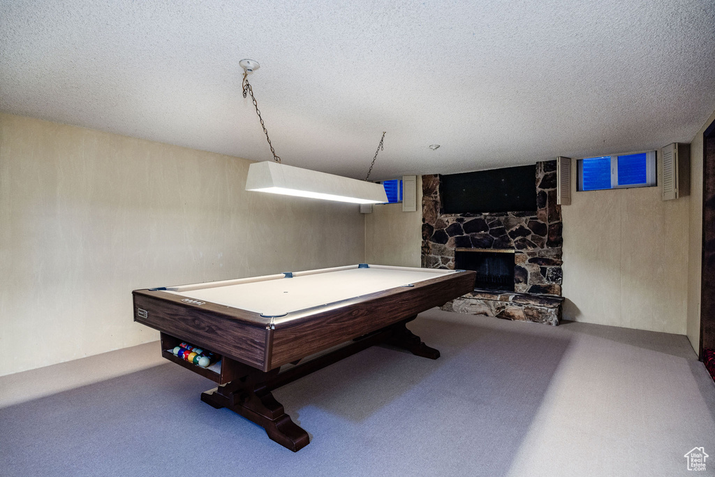 Recreation room featuring billiards, a textured ceiling, a stone fireplace, and carpet