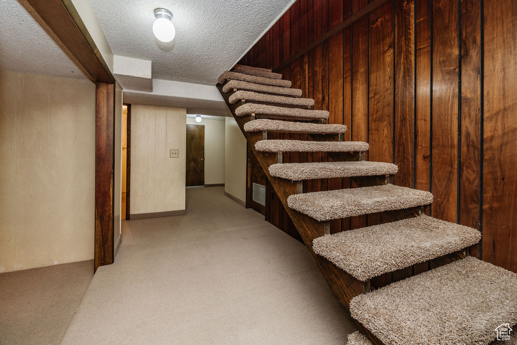 Stairway with wood walls, a textured ceiling, and carpet flooring