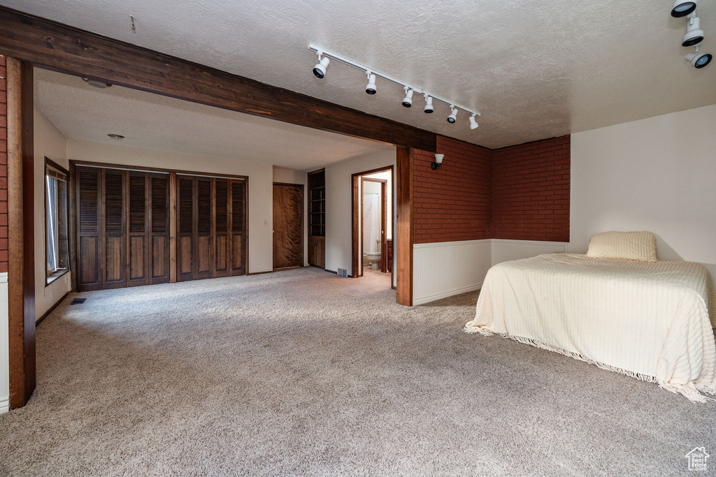 Unfurnished bedroom with beam ceiling, a textured ceiling, track lighting, and light colored carpet