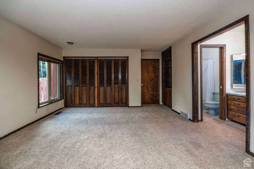 Unfurnished bedroom featuring ensuite bath, a textured ceiling, and light carpet