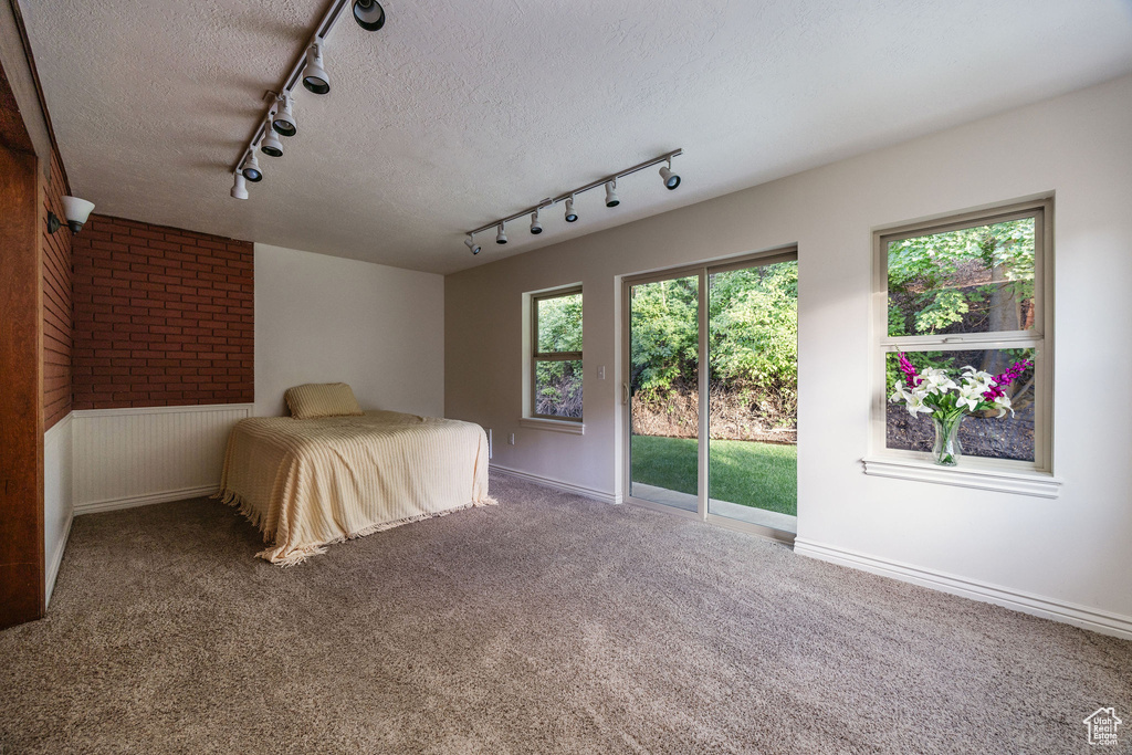 Unfurnished bedroom with access to exterior, a textured ceiling, track lighting, and carpet