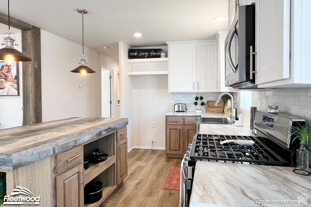 Kitchen featuring appliances with stainless steel finishes, decorative light fixtures, light hardwood / wood-style floors, decorative backsplash, and wooden counters