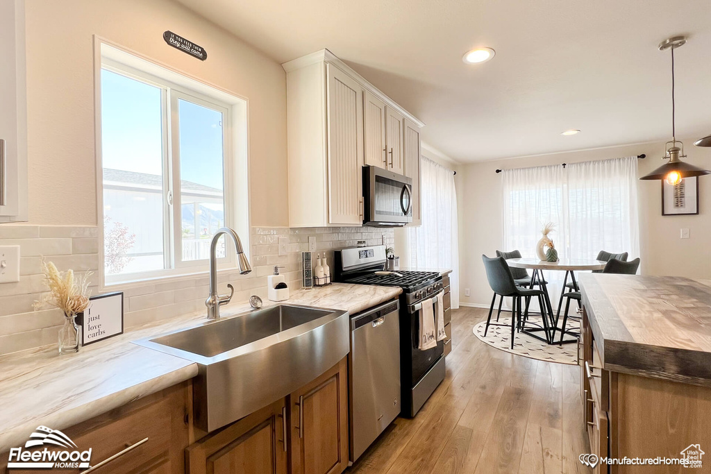 Kitchen featuring backsplash, hanging light fixtures, light hardwood / wood-style floors, sink, and stainless steel appliances