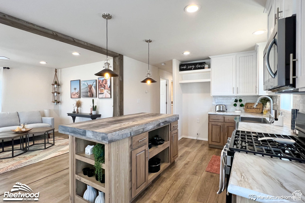 Kitchen with light hardwood / wood-style flooring, a kitchen island, tasteful backsplash, white cabinets, and appliances with stainless steel finishes