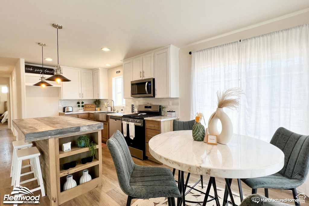 Kitchen featuring appliances with stainless steel finishes, tasteful backsplash, white cabinets, a kitchen island, and hanging light fixtures