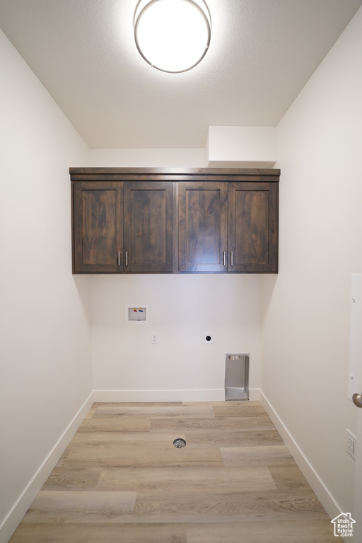 Clothes washing area with light hardwood / wood-style floors, hookup for a washing machine, electric dryer hookup, and cabinets