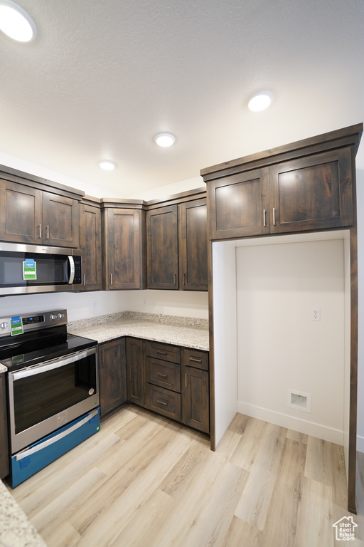 Kitchen with dark brown cabinets, light hardwood / wood-style flooring, light stone countertops, and stainless steel appliances