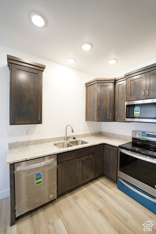 Kitchen with light hardwood / wood-style floors, light stone countertops, sink, stainless steel appliances, and dark brown cabinets