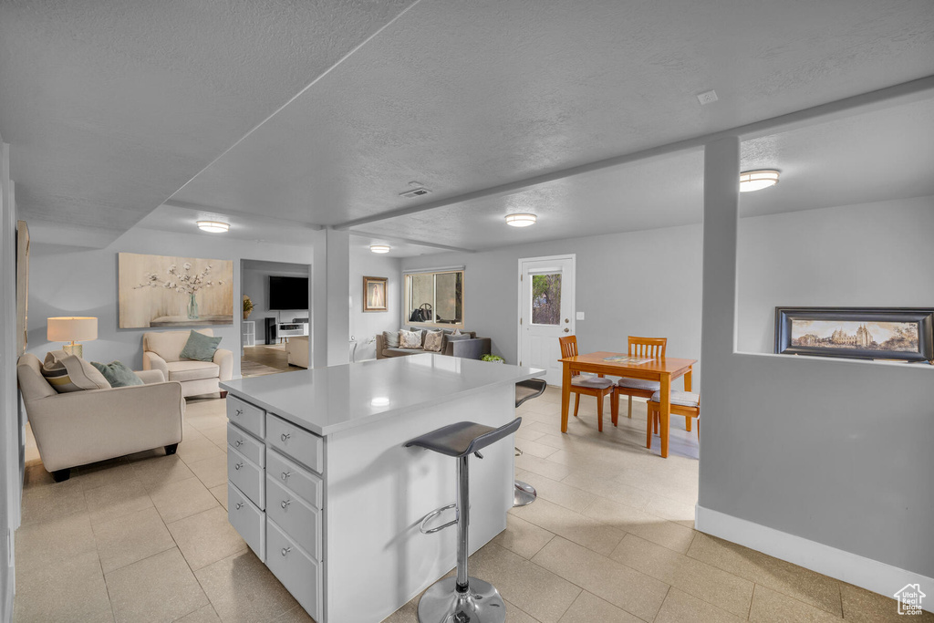 Kitchen with white cabinets, a textured ceiling, a center island, and light tile patterned floors