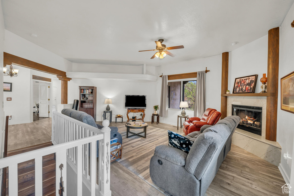 Living room with a fireplace, light hardwood / wood-style flooring, and ceiling fan with notable chandelier