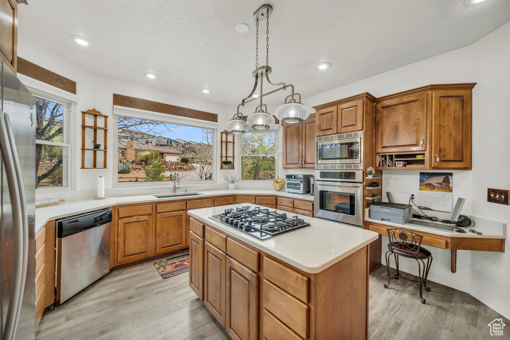 Kitchen with sink, a center island, appliances with stainless steel finishes, light hardwood / wood-style flooring, and hanging light fixtures