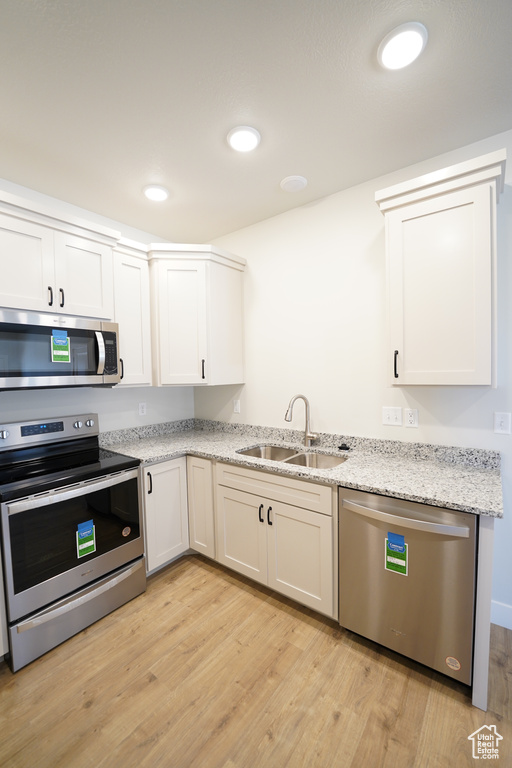 Kitchen featuring light hardwood / wood-style floors, appliances with stainless steel finishes, sink, and light stone countertops