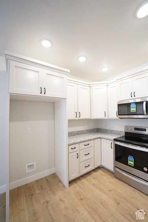 Kitchen featuring stainless steel appliances, white cabinets, light stone counters, and light hardwood / wood-style flooring