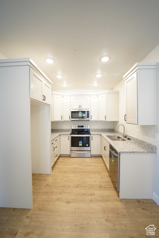 Kitchen with appliances with stainless steel finishes, light hardwood / wood-style flooring, white cabinets, and light stone counters