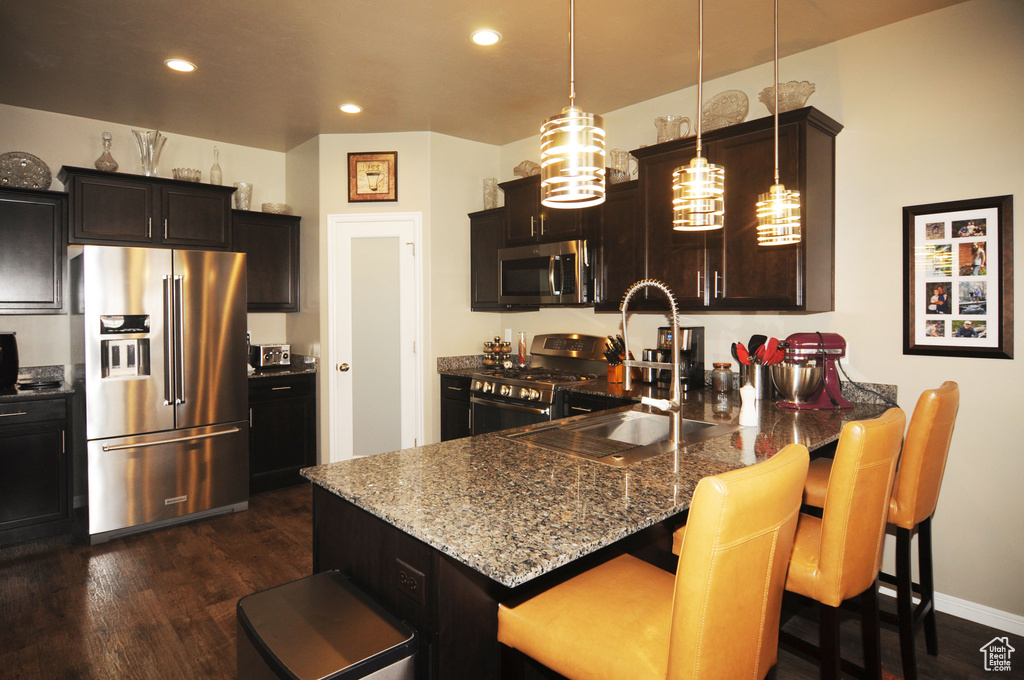 Kitchen with a breakfast bar, appliances with stainless steel finishes, stone countertops, dark hardwood / wood-style floors, and hanging light fixtures