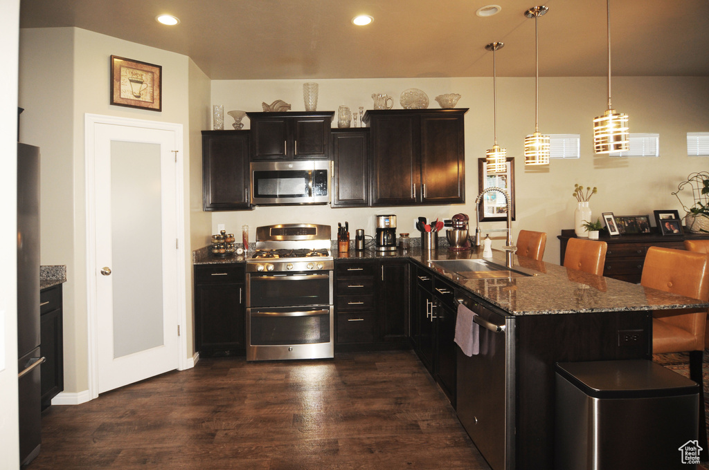 Kitchen with appliances with stainless steel finishes, decorative light fixtures, sink, dark hardwood / wood-style flooring, and a breakfast bar area