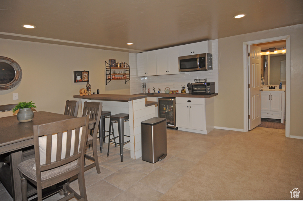 Kitchen with a kitchen bar, wine cooler, tasteful backsplash, light tile patterned floors, and white cabinets