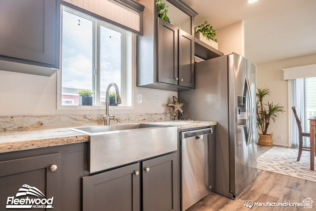 Kitchen with sink, light hardwood / wood-style flooring, stainless steel appliances, and light stone countertops