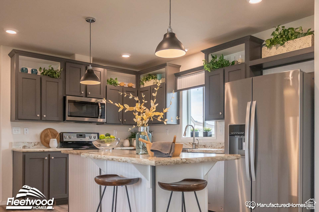 Kitchen with a breakfast bar, stainless steel appliances, pendant lighting, and light stone countertops