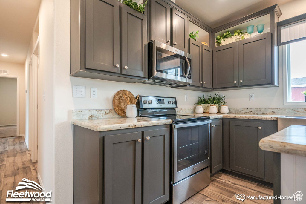 Kitchen featuring light wood-type flooring, appliances with stainless steel finishes, and light stone countertops