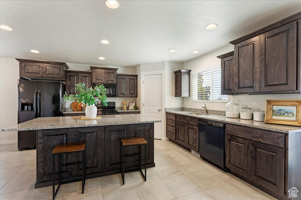 Kitchen featuring a center island, light tile patterned floors, black appliances, and dark brown cabinetry