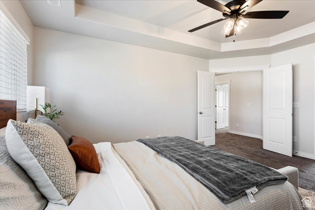 Carpeted bedroom featuring ceiling fan and a tray ceiling