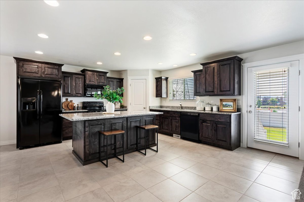 Kitchen with dark brown cabinetry, a healthy amount of sunlight, a kitchen island, and black appliances