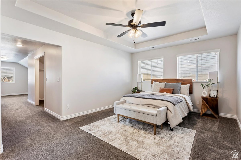 Bedroom featuring ceiling fan, a raised ceiling, and dark colored carpet