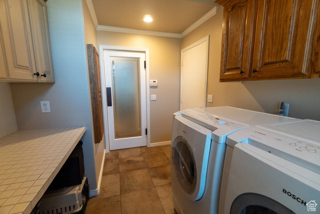 Laundry room with tile patterned flooring, washing machine and dryer, ornamental molding, and cabinets