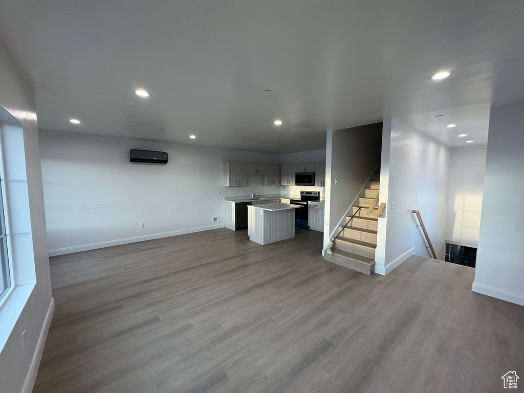 Unfurnished living room with wood finished floors, baseboards, a wall unit AC, and recessed lighting