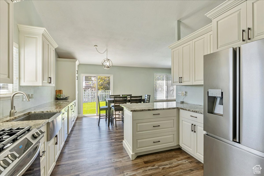 Kitchen with kitchen peninsula, appliances with stainless steel finishes, dark wood-type flooring, and light stone countertops