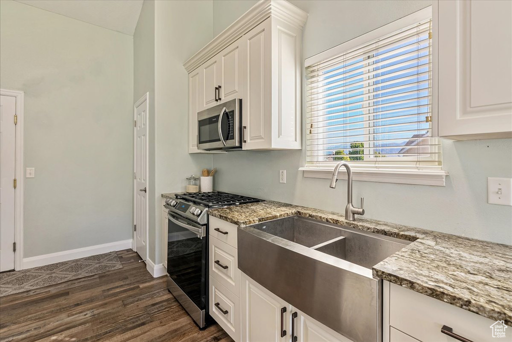 Kitchen featuring appliances with stainless steel finishes, sink, light stone counters, white cabinets, and dark wood-type flooring