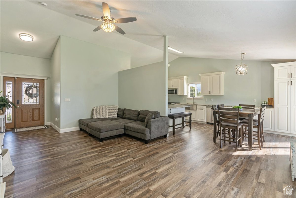 Living room with ceiling fan with notable chandelier, dark hardwood / wood-style floors, sink, and high vaulted ceiling