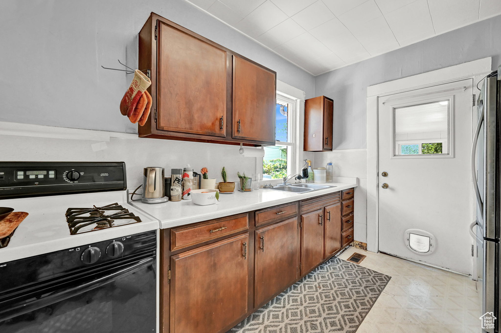 Kitchen with sink, stainless steel refrigerator, light tile patterned floors, and white gas range