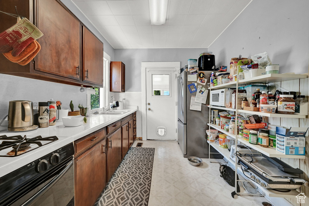 Kitchen featuring white microwave, sink, light tile patterned floors, stove, and stainless steel fridge