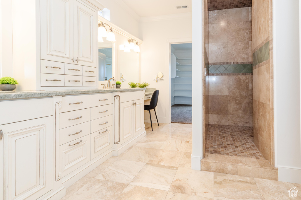 Bathroom with tile patterned flooring, a tile shower, ornamental molding, and vanity