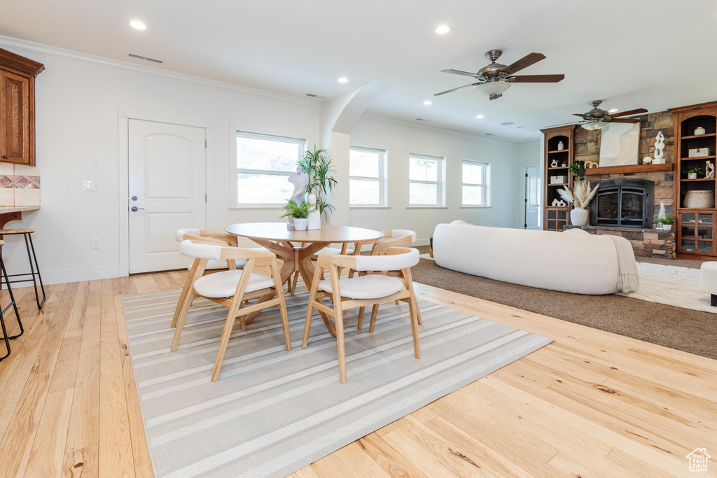 Dining room with ceiling fan, crown molding, light hardwood / wood-style floors, and a stone fireplace