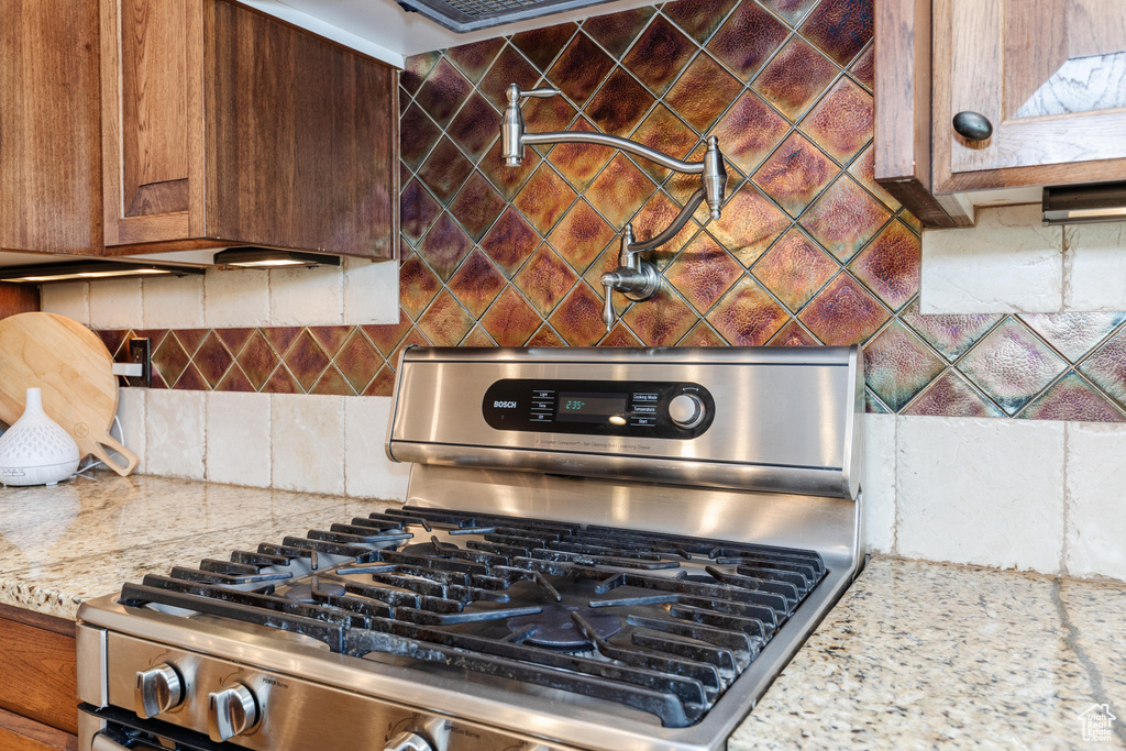 Kitchen with backsplash, stainless steel gas range oven, and light stone counters