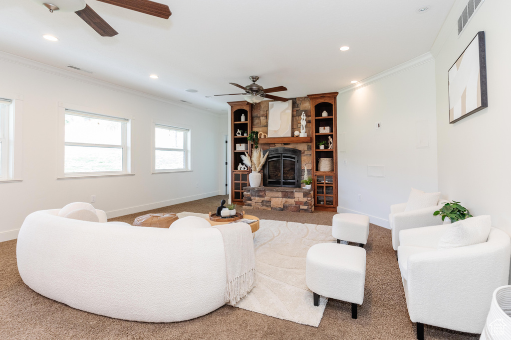 Carpeted living room with ceiling fan, a stone fireplace, and ornamental molding