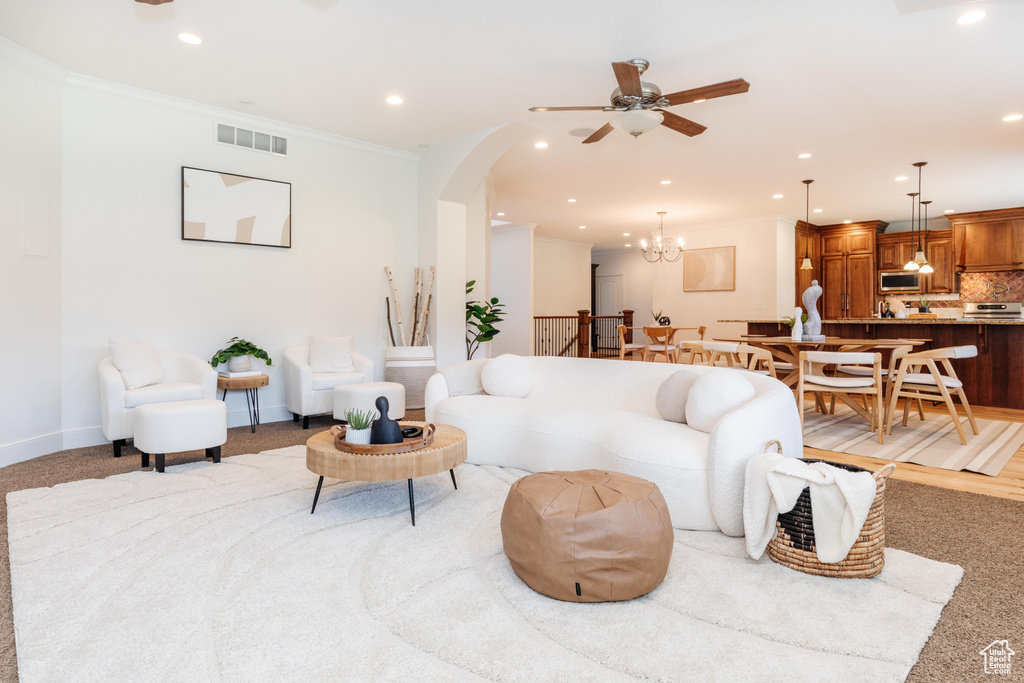 Carpeted living room with crown molding and ceiling fan with notable chandelier