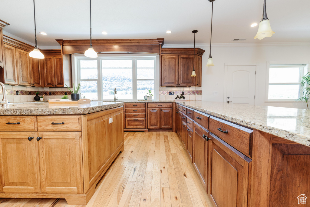 Kitchen with decorative backsplash, crown molding, light hardwood / wood-style floors, and pendant lighting