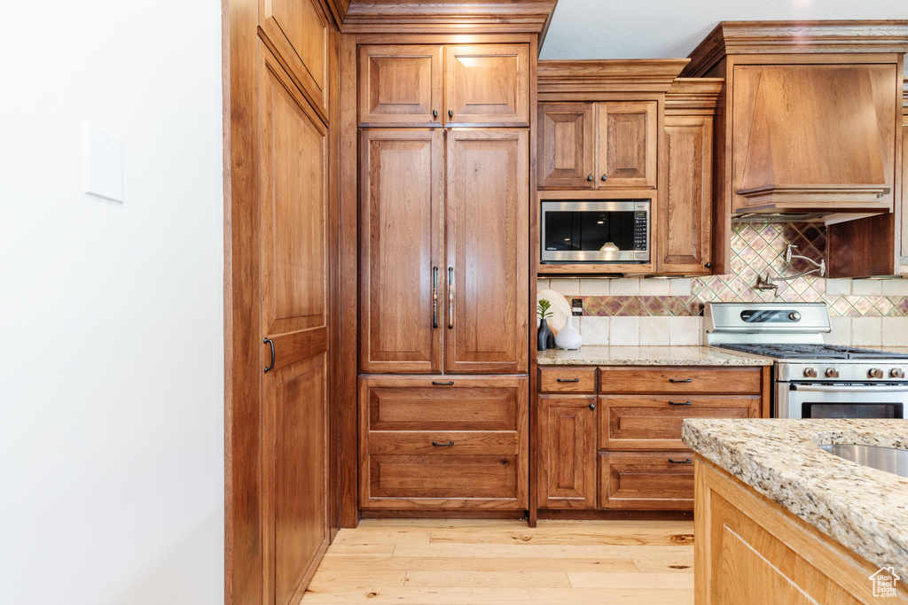 Kitchen featuring light wood-type flooring, backsplash, built in appliances, and light stone countertops