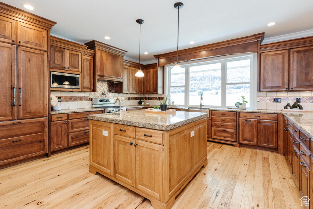 Kitchen with light wood-type flooring, backsplash, a kitchen island with sink, appliances with stainless steel finishes, and light stone counters