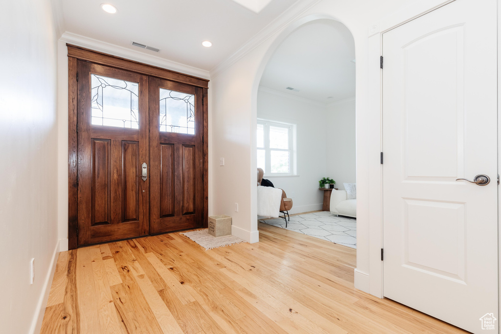 Foyer entrance with crown molding and light wood-type flooring